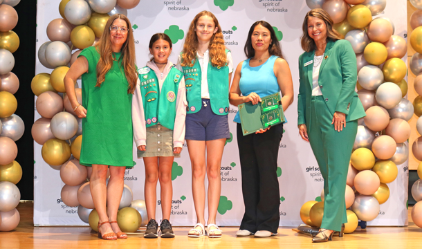 three adults and two Girl Scouts in their uniform standing in front of a colorful display of balloons