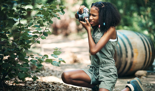 A girl kneeling outside taking a photo of a bush