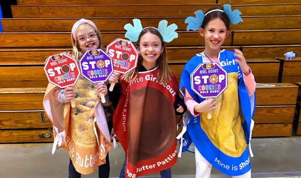 three girls in colorful cookie costumes holding small signs that say "Girl Scout STOP cookies sold here"