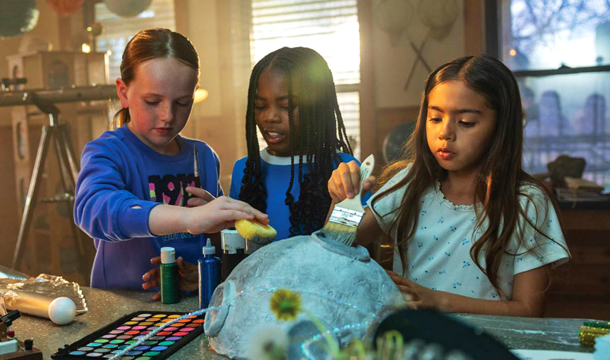 three girls painting a paper maché model of the moon