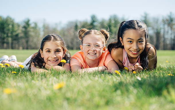 three happy girls laying down in a grassy field