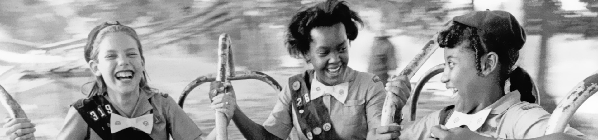  a vintage photo of three girls riding a merry-go-round smiling and laughing 