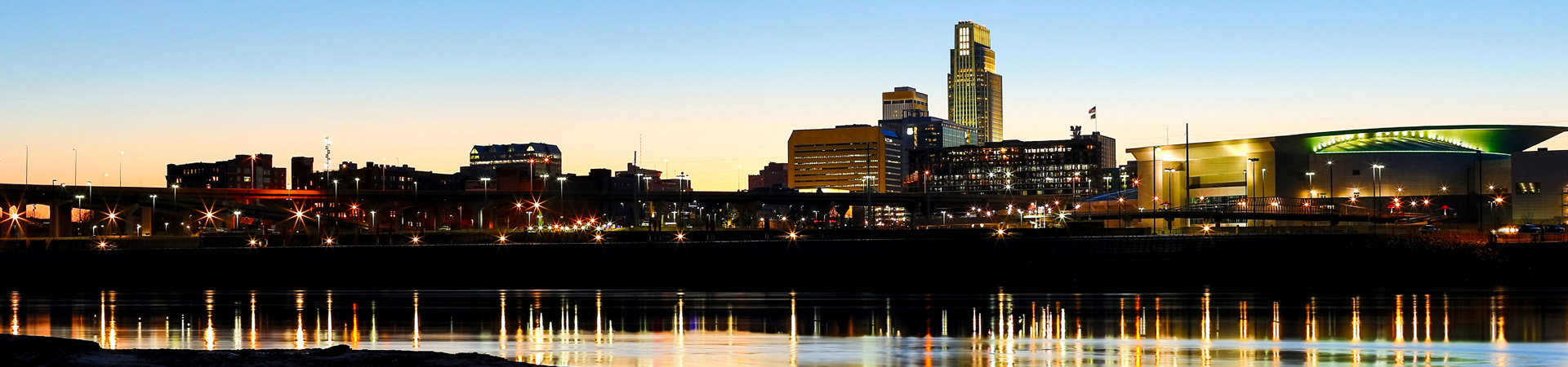 a panoramic photo of the Omaha riverfront looking towards the lights of downtown at night 