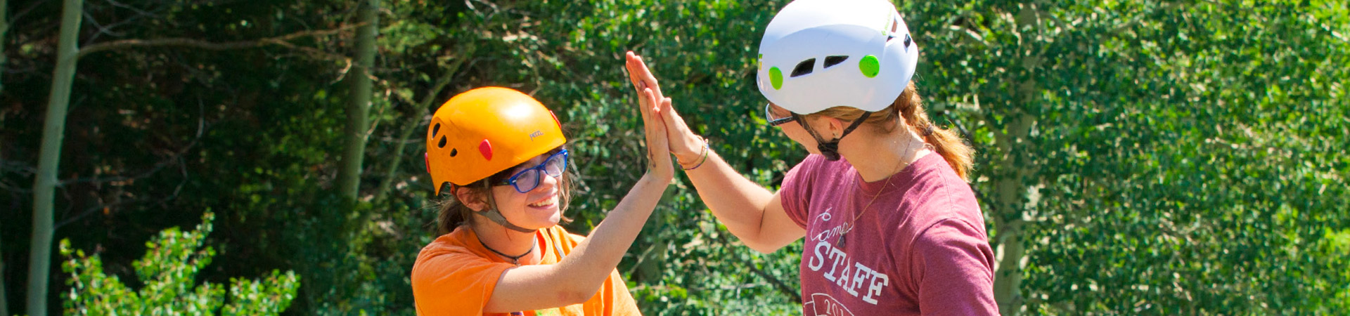  a teenager and a girl scout staff member wearing helmets and giving each other a high five 