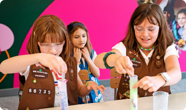 Two girls adding ingredients to their graduated cylinder beakers on top of a white lab table
