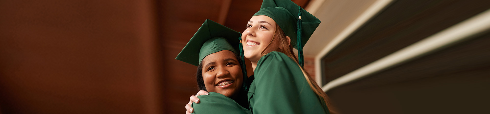  two high school girl scouts in graduation robes hugging and smiling 