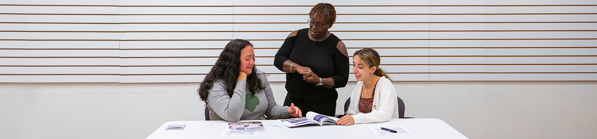  three adult volunteers gathered around a table talking and looking at printed materials 