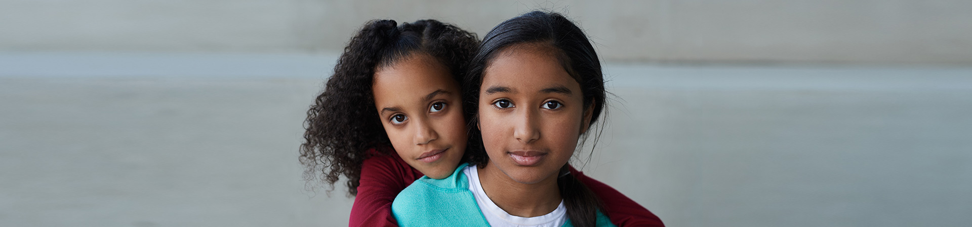  a young girl holding onto an older girl from behind 