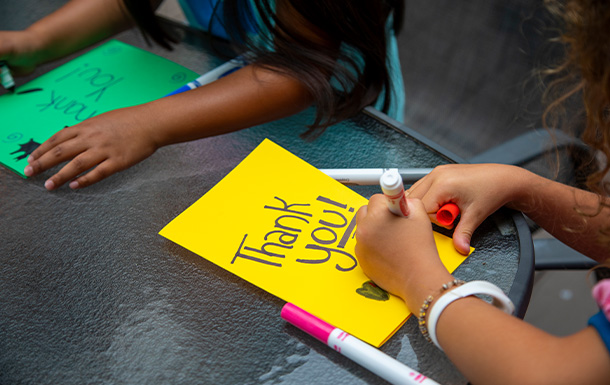 a close up detail of two girls working on brightly colored hand made thank you cards